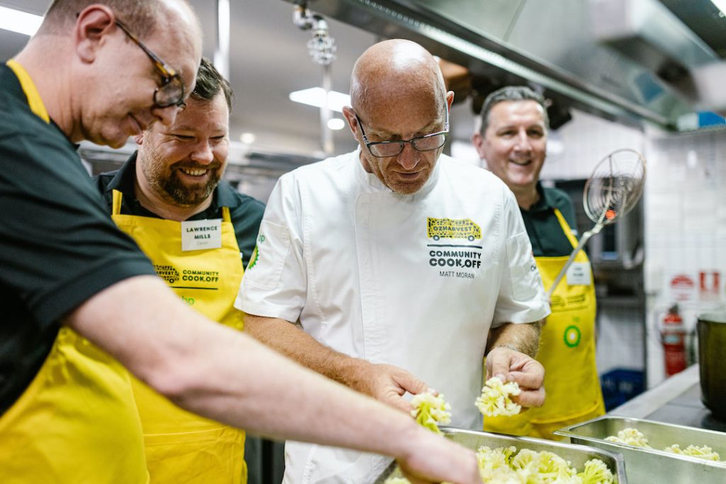 Matt Moran and three other men behind him analyzing the vegetables they are to use to make meals for the OzHarvest CEO CookOff.